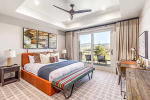 Bedroom with access to exterior, a tray ceiling, light colored carpet, and a ceiling fan