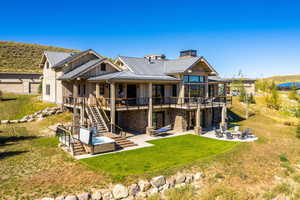 Rear view of house featuring a lawn, stairway, a patio area, metal roof, and stone siding