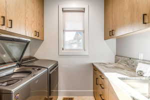 Clothes washing area with cabinet space, washing machine and dryer, baseboards, and a sink