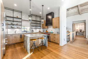 Kitchen featuring open shelves, tasteful backsplash, light wood-style flooring, wall chimney range hood, and high end stove