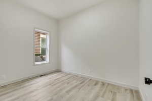 Empty room featuring light wood-style floors, visible vents, and baseboards