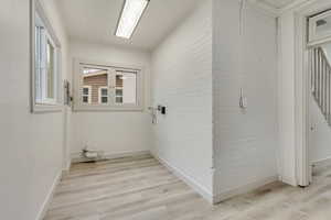 Laundry area featuring brick wall, light wood-style flooring, and baseboards