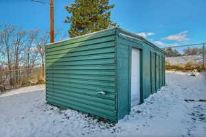 Snow covered structure with a shed, an outdoor structure, and fence