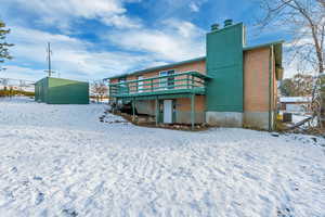 Snow covered back of property featuring a deck, brick siding, and a chimney