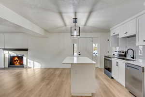 Kitchen featuring tasteful backsplash, a kitchen island, appliances with stainless steel finishes, light wood-type flooring, and a sink