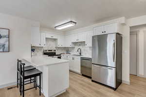 Kitchen featuring a breakfast bar area, a peninsula, stainless steel appliances, white cabinetry, and a sink