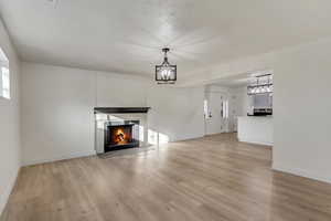 Unfurnished living room featuring baseboards, a lit fireplace, an inviting chandelier, and light wood-style floors