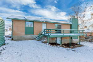 Snow covered rear of property featuring a deck, brick siding, and a chimney