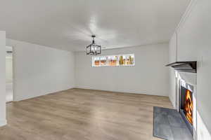 Unfurnished dining area with a warm lit fireplace, light wood-style flooring, baseboards, and an inviting chandelier