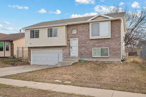 Raised ranch with a garage, brick siding, fence, and driveway