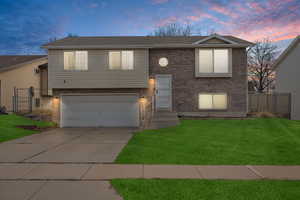 Bi-level home featuring concrete driveway, an attached garage, fence, a front yard, and brick siding