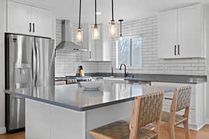 Kitchen with stainless steel appliances, white cabinetry, wall chimney range hood, and decorative backsplash