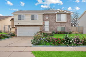 Split foyer home featuring brick siding, concrete driveway, fence, a garage, and a front lawn