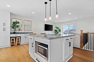 Kitchen featuring light wood-type flooring, open floor plan, stainless steel microwave, and white cabinets