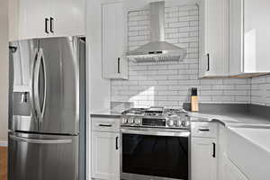 Kitchen featuring wall chimney range hood, white cabinetry, stainless steel appliances, and backsplash