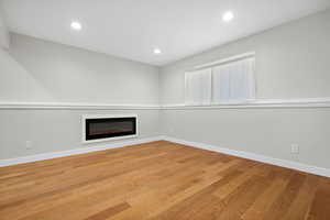 Unfurnished living room with light wood finished floors, a glass covered fireplace, and baseboards