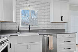 Kitchen featuring white cabinets, decorative backsplash, hanging light fixtures, stainless steel appliances, and a sink