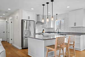 Kitchen featuring a sink, wall chimney range hood, light wood-type flooring, and stainless steel fridge