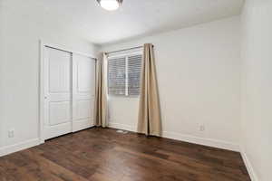 Unfurnished bedroom with dark wood-style floors, a closet, visible vents, and baseboards