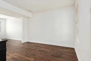 Empty room featuring dark wood-style floors, visible vents, and baseboards