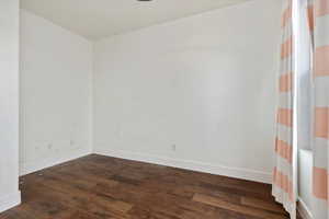 Spare room with baseboards and dark wood-type flooring