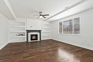 Unfurnished living room featuring baseboards, visible vents, dark wood-type flooring, built in shelves, and a high end fireplace