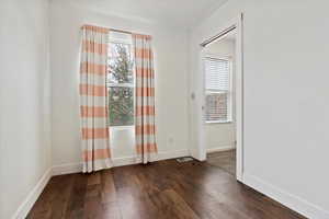 Empty room featuring dark wood-style floors, visible vents, and baseboards