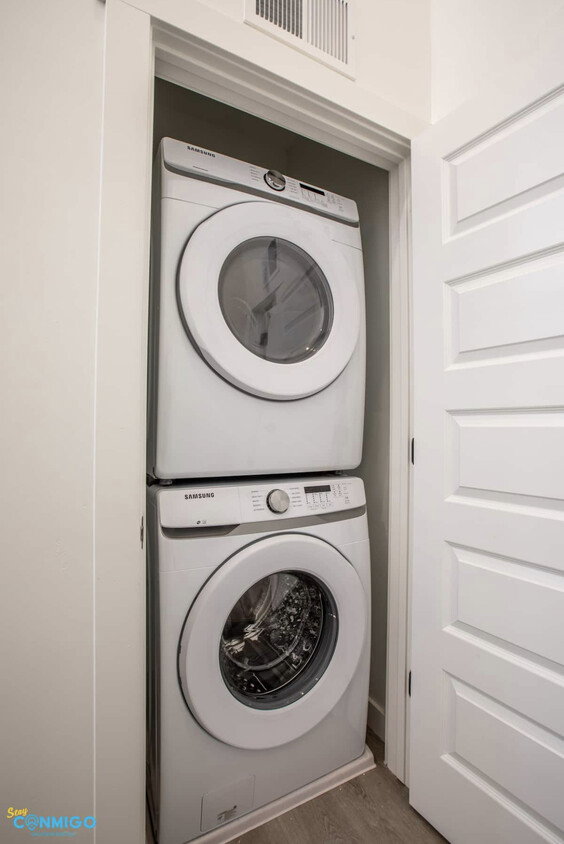 Clothes washing area with laundry area, visible vents, stacked washing maching and dryer, and wood finished floors