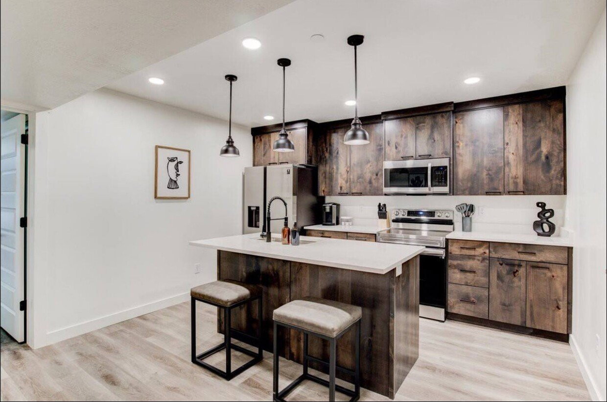 Kitchen with a breakfast bar, stainless steel appliances, light countertops, a kitchen island with sink, and dark brown cabinetry