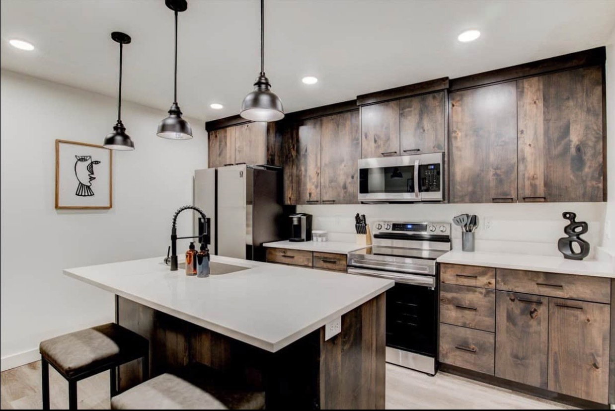 Kitchen with a kitchen island with sink, stainless steel appliances, a sink, light countertops, and light wood finished floors