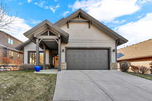 Craftsman-style house with stone siding, driveway, a garage, and a front yard