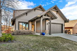 View of front of property featuring stone siding, concrete driveway, a front lawn, and an attached garage
