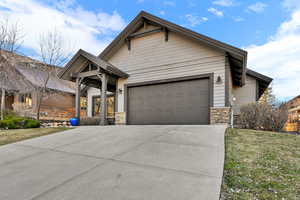 Craftsman-style house featuring stone siding, driveway, a garage, and a front yard