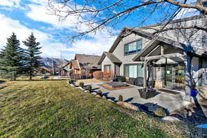 Rear view of house with a patio, a yard, and stone siding