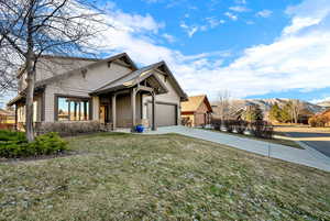 View of front of property featuring stone siding, driveway, a front yard, and an attached garage