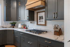 Kitchen with premium range hood, gas cooktop, upgraded cabinetry, and quartz countertops.