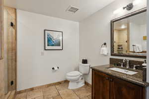 Full bathroom featuring baseboards, visible vents, toilet, stone tile flooring, and a shower stall