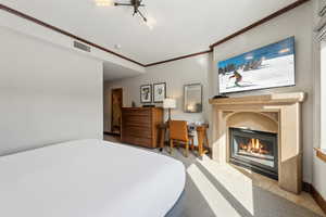 Bedroom featuring crown molding, visible vents, a glass covered fireplace, carpet flooring, and baseboards