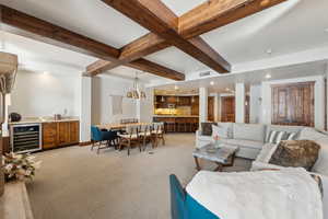 Living area featuring wine cooler, beam ceiling, indoor wet bar, light colored carpet, and visible vents