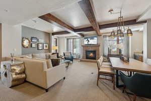 Living area with a textured ceiling, beamed ceiling, a glass covered fireplace, and light colored carpet