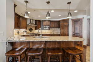 Kitchen with wall chimney exhaust hood, appliances with stainless steel finishes, backsplash, and a sink