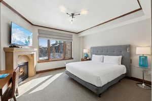 Carpeted bedroom with ornamental molding, a glass covered fireplace, and baseboards