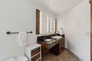 Bathroom featuring stone tile flooring, a sink, baseboards, and double vanity