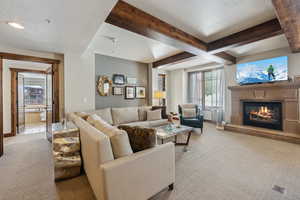 Carpeted living room with a glass covered fireplace, beam ceiling, a textured ceiling, and baseboards