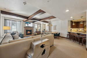 Living area with a textured ceiling, beamed ceiling, a glass covered fireplace, and baseboards