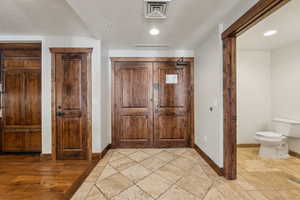 Foyer entrance with visible vents, stone tile floors, a textured ceiling, and baseboards