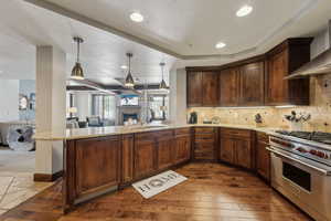 Kitchen featuring open floor plan, a peninsula, premium range, wall chimney range hood, and a sink