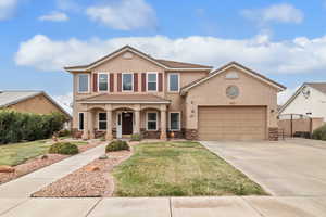 View of front of property with stucco siding, stone siding, driveway, an attached garage, and a front lawn
