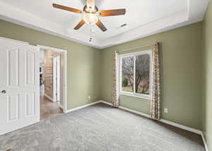 Unfurnished bedroom with carpet floors, a tray ceiling, baseboards, and a ceiling fan