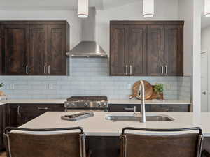 Kitchen featuring wall chimney exhaust hood, dark brown cabinets, a sink, and gas stove